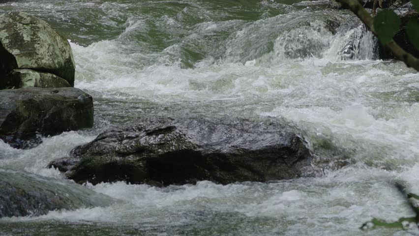 Large natural torrent flowing between rugged rocky surface with green forest foliage in the foreground.