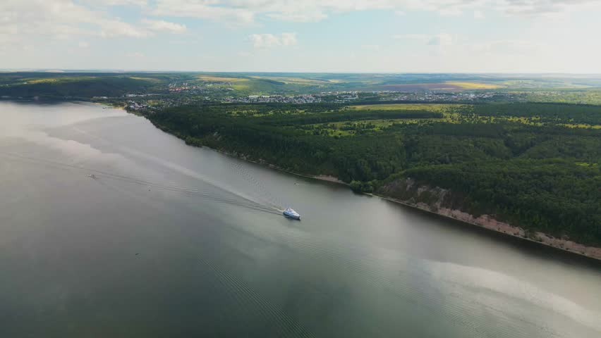 the ship goes through the water of the river forming waves. Top view of the wide river, forest and fields
