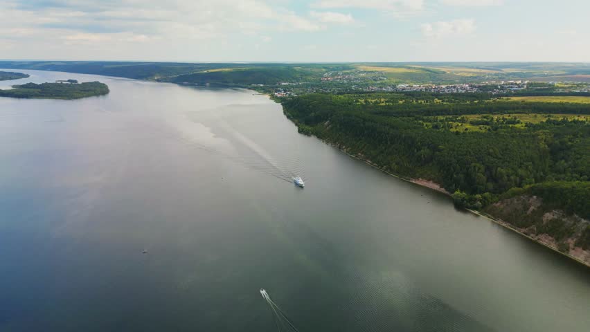 the ship goes through the water of the river forming waves. Top view of the wide river, forest and fields