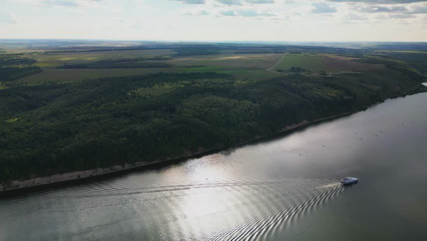 the ship goes through the water of the river forming waves. Top view of the wide river, forest and fields