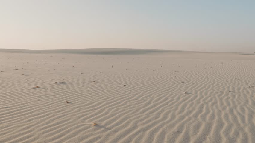 A woman in a flowing pink dress walks barefoot across vast white sand dunes, leaving footprints behind. The serene landscape and soft light create a peaceful, cinematic, and elegant visual.