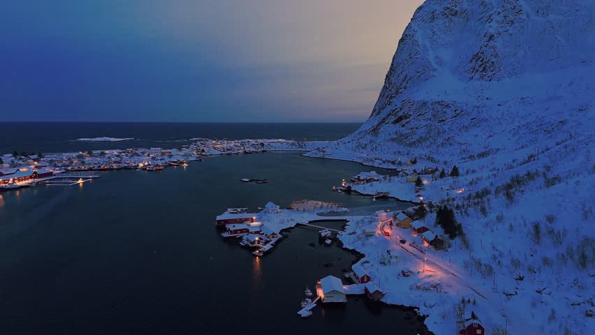 Snow-covered Reine village in Lofoten, Norway at twilight, surrounded by mountains and fjords
