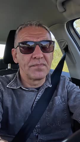 Middle-Aged Man with Sunglasses Driving a Car. Front view of handsome, mature man in vehicle interior, enjoying road trip. Portrait of elegant, relaxed driver in a comfortable car seat during commute.