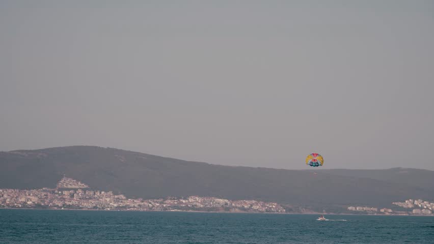 Double parasail over stunning coastline, admiring bright blue sea and distant city under clear sky. Soar through air and create unforgettable memories in this beautiful setting