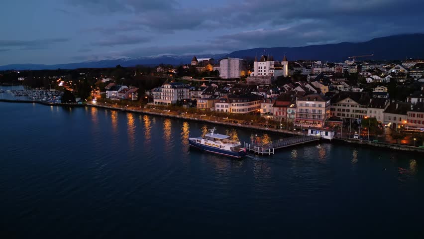 Orbit drone shot of white boat leaving Nyon Port at sunrise on Lake Geneva in Switzerland