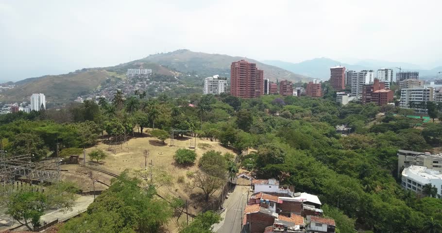 Aerial view towards the mountains, with a green area near large buildings in Cali, Colombia, capturing the blend of nature and urban life in a sunny setting