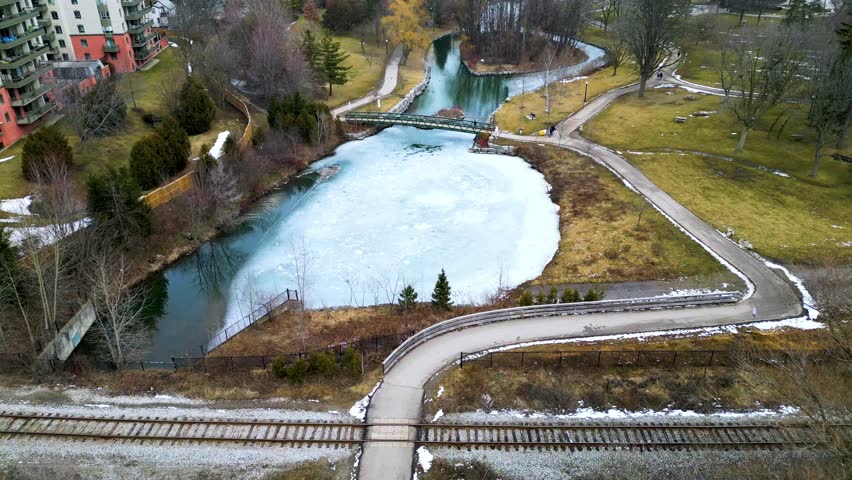 Low level wide angle aerial view of Victoria Park in Kitchener Waterloo during the winter. The tree branches are barren and the water surface is mostly ice covered.