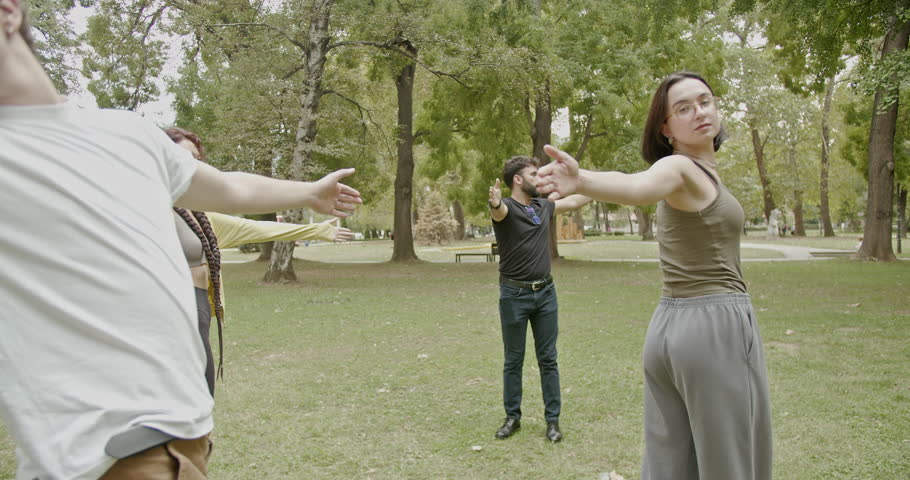 Students attending a sport class in the park with their professor. They are doing various stretches and warm-up exercises.