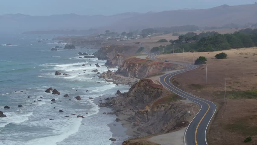 Aerial medium pullback above winding coastal cliffside road of PCH Highway 1 on misty overcast day