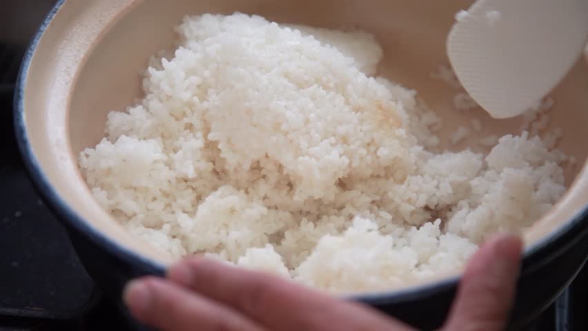 A woman mixing rice cooked in a clay pot
