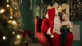 A joyful boy sits on Santas lap, surrounded by a beautifully decorated Christmas tree, while Santa holds a baby - Powered by Shutterstock - Get 15% off with code: PIKWIZARD15