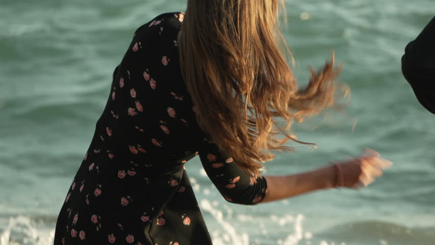 Woman Beach Dress Waves - A woman in a polka-dot dress stands on a beach with waves crashing in the background.
