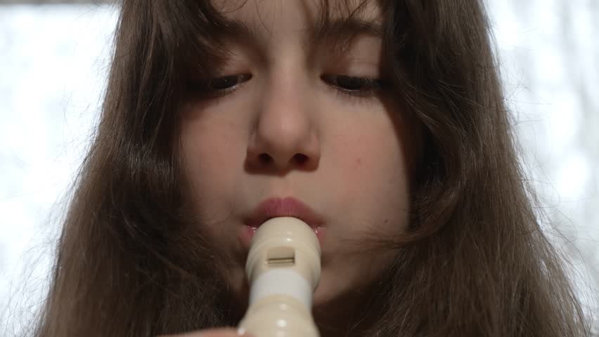 A teenage girl is playing a recorder flute. Close-up