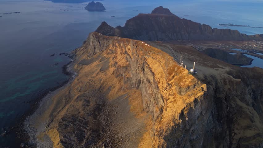 As the winter day fades into twilight, the sun's warm glow bathes the mountains and the sea on Vaeroy in Lofoten, Norway.