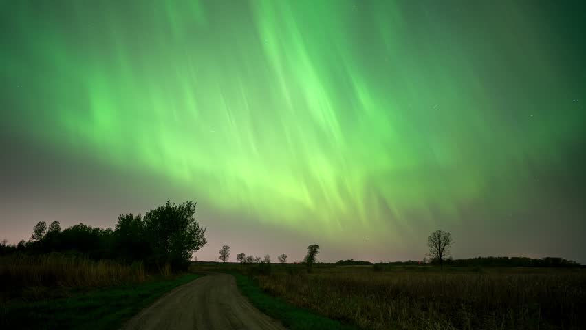 Bright green northern lights illuminating the night sky above a rural country road in Minnesota, USA.