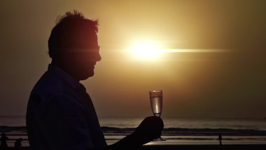 Silhouette of a person making a toast with a drink against a sunset backdrop in slow motion 250fps