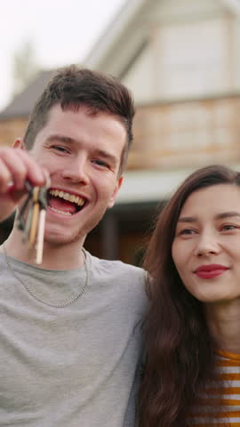 Young married couple or family buy a new house. Happy man and woman or owners shake key in air and hug each other in front of their newly bought home. Excited clients purchasing estate or apartment