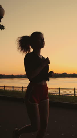 Silhouette of a beautiful asian girl run along the river. Taste of freedom. Playing sports at sunrise or sunset. Solo activity or running alone. Concept of workout, jogging, training, cardio.