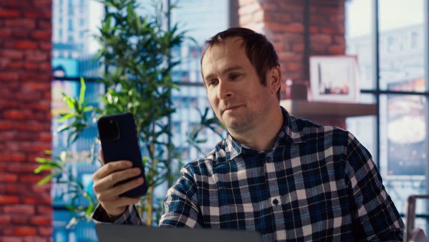 Joyous freelancer in home office sitting at desk in front of laptop, greeting colleagues in videocall. Cheerful employee in teleconference meeting with managers, answering inquiries, camera B