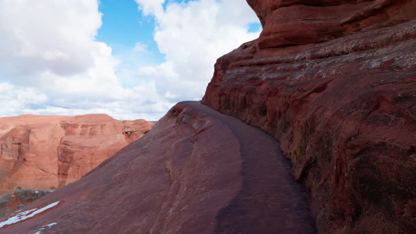 Push in shot following a narrow hiking path toward the edge of a cliff in Arches National Park Utah on a sunny day.