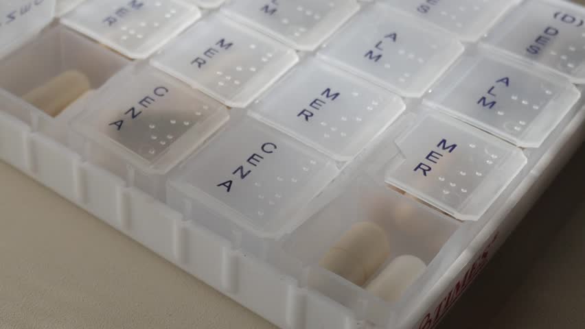 Close up of a pill box with different minerals, vitamins inside, organizing the taking of supplement, truck shot on slow motion