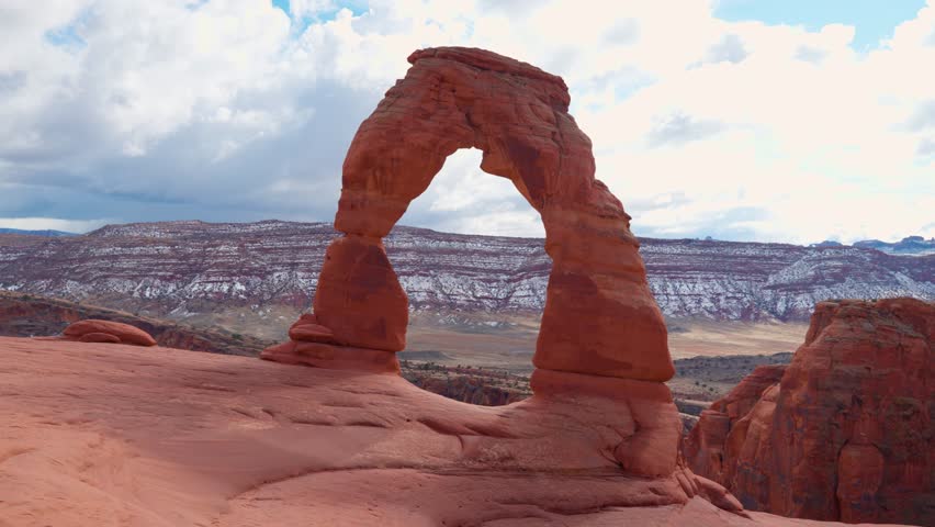 Wide shot of Delicate Arche at the top of the mountains in arches national park as a bird flies Infront briefly.