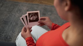 African American mom mother pregnant woman with big belly tummy pregnancy girl female at home couch clinic hospital sofa holding looking at usd pictures photo ultrasound diagnosis scan medicine health - Powered by Shutterstock - Get 15% off with code: PIKWIZARD15