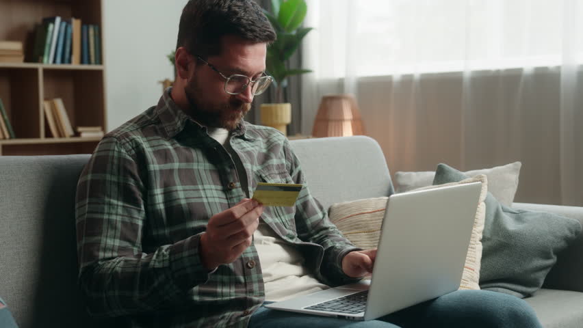 Caucasian man male guy at home happy smiling holding credit bank card buying online internet banking pay purchase shopping buying payment success achieve with laptop computer showing thumb up order