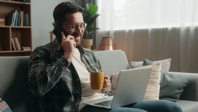 Caucasian man male guy at home happy smiling positive talking mobile phone call friendly communicate smartphone conversation drinking tea holding cup looking laptop computer couch order food delivery - Powered by Shutterstock - Get 15% off with code: PIKWIZARD15