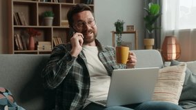 Caucasian man male guy at home happy smiling positive talking mobile phone call friendly communicate smartphone conversation drinking tea holding cup looking laptop computer couch order food delivery - Powered by Shutterstock - Get 15% off with code: PIKWIZARD15