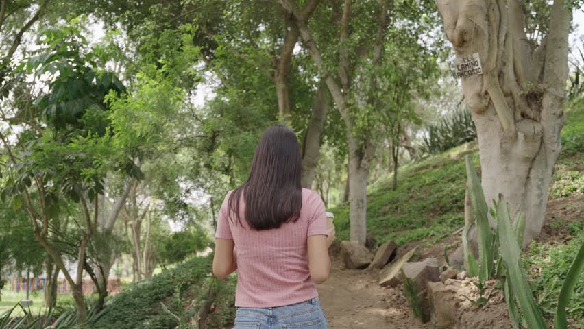Slow motion of a young woman walking alone on a path through a tranquil forest, enjoying the peaceful atmosphere