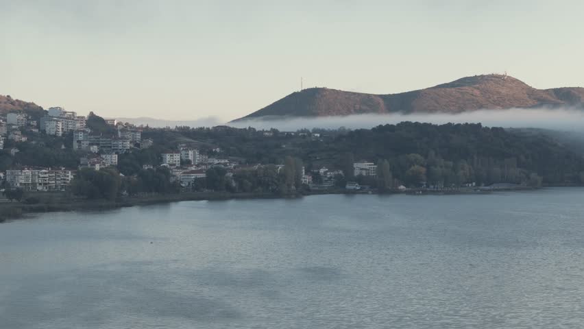 Drone shot, flying towards the fog, scene above the lake, overcast mist over the hill, winter climate, blue water sea. 4k video