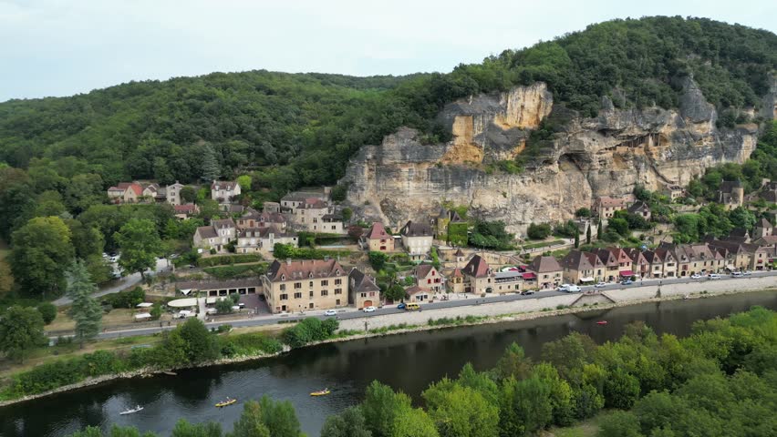 Drone aerial view in France countryside small old medieval town below a stone cliff surrounded by a green forest and a river circling around in La Roque Gageac
