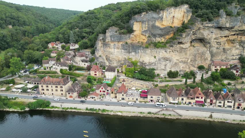 Drone aerial view in France countryside small old medieval town below a stone cliff surrounded by a green forest and a river circling around in La Roque Gageac
