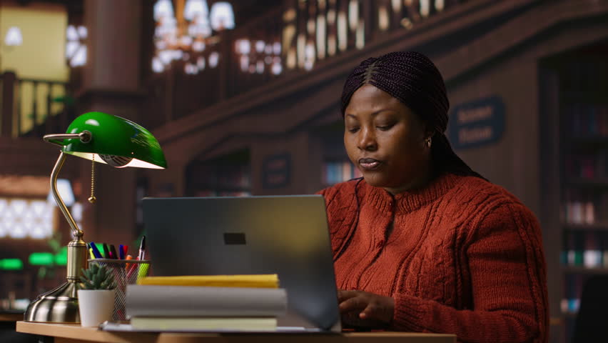 African american tutor preparing documents and learning materials for teaching session in school library. Clever professor providing academic resources for mentoring in the study area. Camera B.