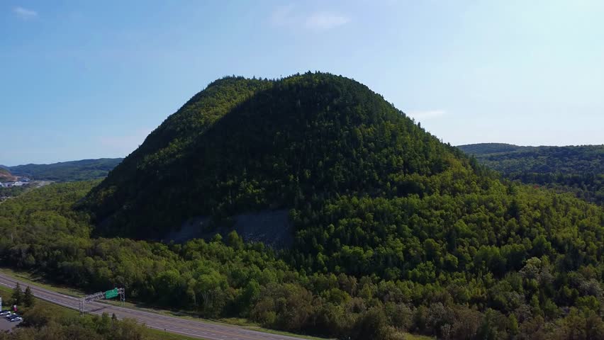 Aerial view of Sugarloaf Mountain, an ancient volcano located in Atholville, New Brunswick, with Chaleur Bay and the city of Campbellton in the background under a blue sky.