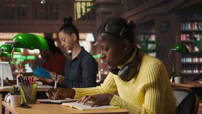 Young focused scholar doing her homework at a library desk after classes, engrossed in literature and notes. Pupil completing her notes in the copybook, productive study sessions. Camera A. - Powered by Shutterstock - Get 15% off with code: PIKWIZARD15