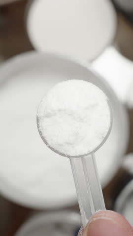 Vertical video. Athlete pouring Creatine powder back into the container, adjusting the amount for the correct supplementation dose. Slow motion.