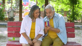 Happy senior couple using smart phone at summer park. Watching video, Social media. Online Entertainment. Wireless Technology. Fast internet 5G network.   - Powered by Shutterstock - Get 15% off with code: PIKWIZARD15