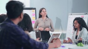 Young attractive businesswoman or female corporate executive delivering a presentation or speech in conference room meeting with diverse group of office colleagues or coworkers in a start up business - Powered by Shutterstock - Get 15% off with code: PIKWIZARD15