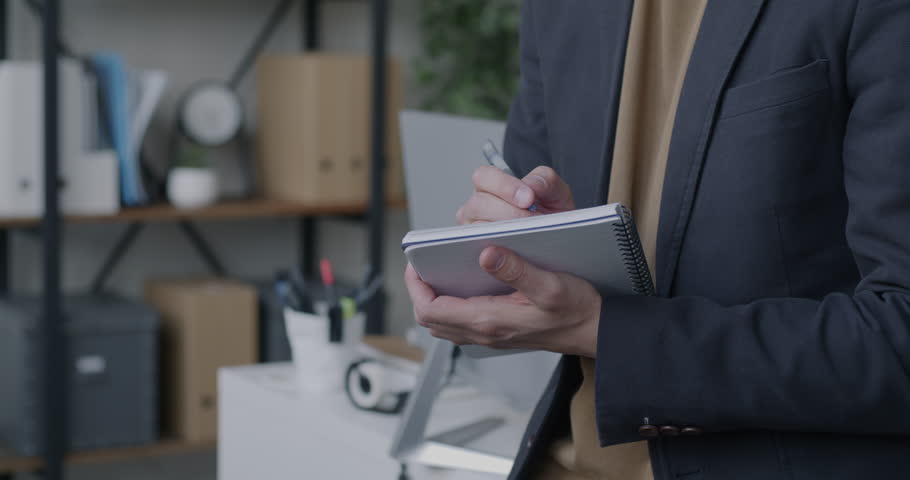 Close-up of male hand writing in notebook while businessman working in office. Professional information and man taking notes concept.