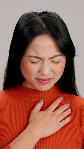Sick, asian woman and chest pain with asthma, breathing difficulty or sore lungs on a studio background. Female person, model or influenza with heartburn, discomfort or inflammation for tuberculosis