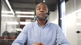 Confident african american businessman in wireless headset talking on a video call looking at camera sitting in office. Entrepreneur has a business meeting. Coach speaks remotely at online training - Powered by Shutterstock - Get 15% off with code: PIKWIZARD15