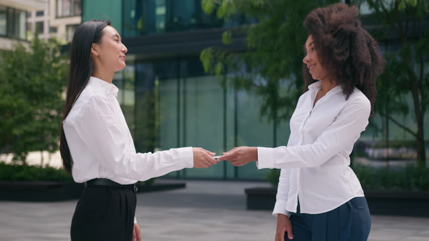 African American woman giving business card Asian Korean women businesswomen partnership advertisement entrepreneur insurance company clients city outdoors specialist lawyer saleswoman work girls town