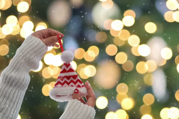 Woman hands holding christmas hat decoration over Christmas tree bokeh background.