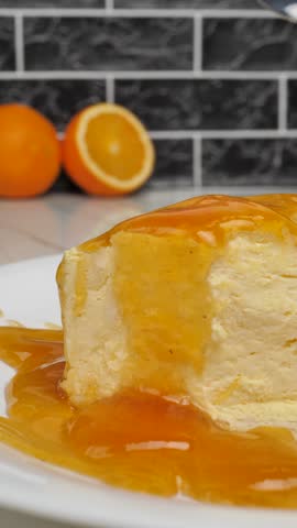 Vertical: Metal shiny spoon take a piece of soft ice cream with yellow citrus jelly syrup. Use spoon take soft mousse dessert with orange flavor on plate. Delicious fruit mousse with pieces of fruit