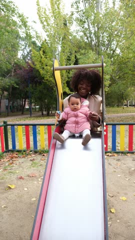 Happy african american mother helping her baby daughter going down a slide