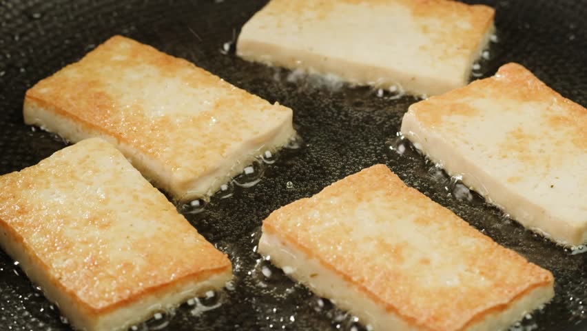 Fried tofu with sesame seeds and spices on cast iron pan, cooking japanese salad. Healthy ingredient for cooking vegan vegetarian diet food. Roasted tofu over black background.