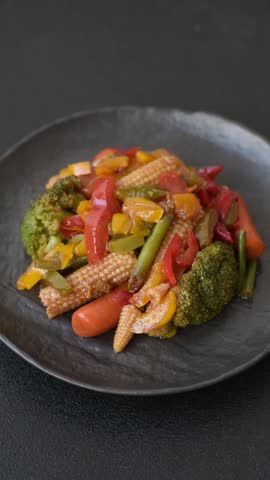Mix of vegetables corn, carrots, peppers, broccoli, onions in teriyaki sauce on a ceramic plate on a dark concrete background