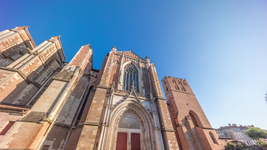 Saint Etienne Cathedral in Toulouse timelapse hyperlapse. Details of the north facade of church. Sunset shadows cover its walls, with a green park in front and a blue sky above. France.